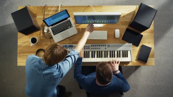 Вид зверху на двох звукорежисерів, що працюють у своїй сонячній студії. Вони грають на музичній клавіатурі і експериментують зі звуком . — стокове відео