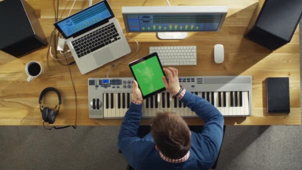 Draufsicht eines Musikers, der während der Arbeit in seinem Studio einen grünen Tablet-Computer in der Hand hält. sein Arbeitsplatz ist High-Tech, aber auch sonnig und warm. — Stockvideo