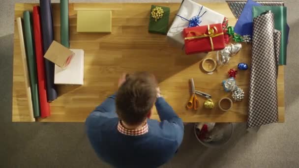Vue du dessus du jeune homme emballant habilement des cadeaux colorés. Tout se passe en mouvement rapide . — Video