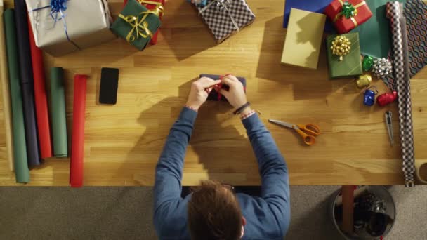 Vue du dessus du jeune homme emballant habilement des cadeaux colorés dans son studio ensoleillé . — Video