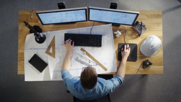Vue du dessus d'un ingénieur technique travaillant sur ses plans, plans de dessin, utilisant un ordinateur de bureau. Divers objets utiles allongés sur sa table . — Video