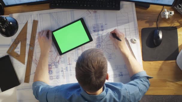 Top View of Architectural Engineer Draws on His Blueprints, Compares with Tablet Computer with Green Screen, Using Desktop Computer Also. His Desk is Full of Useful Objects and Morning Sun. — Stock Video