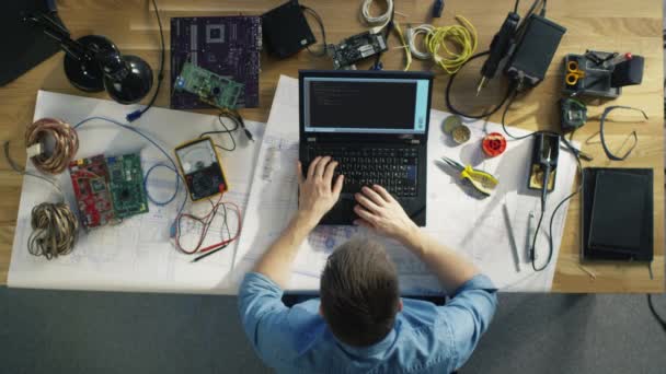 Ovanifrån av en begåvad det teknikern skriva koden på sin Laptop som sitter vid sitt skrivbord, han är omgiven av olika tekniska komponenter. Solen skiner på hans skrivbord. — Stockvideo