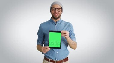Orta bir kadeh bir şapka ve gözlük bize izole yeşil ekran Tablet bilgisayarınızla sunan şık bir genç adam. Beyaz bir arka plan üzerinde ateş.