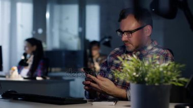 Geç gece ofiste. Adam onun Resepsiyon, muayenelere Smartphone, yazar bir not aşağı oturur. Arka planda çalışma onun arkadaşları.