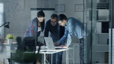 Gece geç saatlerde takım tasarım mühendisleri büyük konferans masası yerinde bir proje üzerinde çalışma. Onlar görüş ve belgelerdeki düzeltmeler yapmak değişimi. Tablo aydınlatılmış.