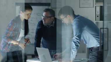 Gece geç saatlerde takım tasarım mühendisleri büyük konferans masası yerinde bir proje üzerinde çalışma. Onlar görüş ve belgelerdeki düzeltmeler yapmak değişimi. Tablo aydınlatılır. Ağır çekimde atış.