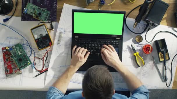 Top bekijken van een Gifted technicus typen op zijn Green Screen Laptop zittend op zijn bureau, hij is omringd door verschillende technische onderdelen, concepten. Zon schijnt op zijn Bureau. — Stockvideo