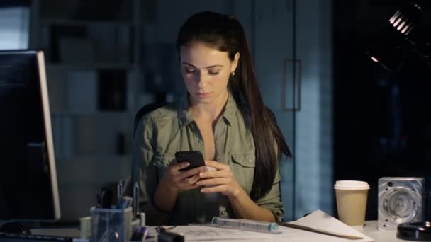 Sent på natten Design ingenjör fungerar på hennes utkast och system, innehar Smartphone. Office är upplyst av hennes bordslampa. — Stockvideo
