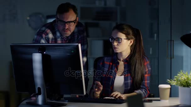 Tarde noche en la oficina. Colegas y Colegas discuten trabajo hecho en su computadora personal. En el fondo El hombre trabajando en su escritorio . — Vídeo de stock