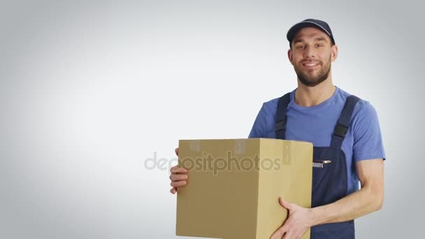 Средний снимок симпатичного погрузчика, держащего картонную коробку. Молодой человек стоит в изоляции на белом фоне . — стоковое видео