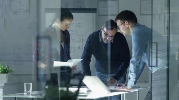 Tarde en la noche Equipo de Ingenieros de Diseño Trabajar en un proyecto. Trabajan en una mesa de conferencias iluminada con documentos, planos y computadora portátil . — Vídeo de stock