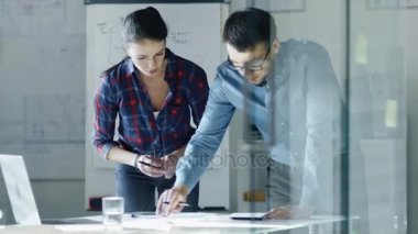 Erkek ve dişi tasarım mühendisleri taslaklar üzerinde çalışmak, düzeltmeleri yapın ve onların projeyi tartışmak. Arka plan üzerinde beyaz tahta çizimler ile standları.