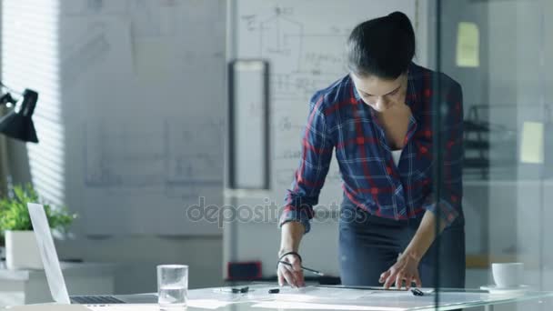 No final da noite, a engenheira de design feminina trabalha em documentos, rascunhos com régua de escala do engenheiro. Na sala Whiteboard com esboços sobre ele, nas paredes Pinned Blueprints . — Vídeo de Stock