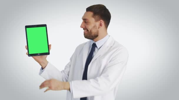 Середній знімок гарного лікаря, який тримає планшетний комп'ютер з однією рукою і робить спливаючі, торкаючись жестів з іншою. Планшет має зелений екран. Знімок з білим тлом . — стокове відео