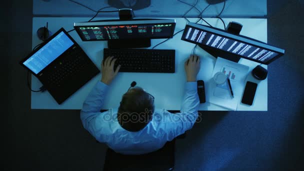 顶视图的一个成功的股票经纪人监测市场波动和成为大赢家。两台显示器和一台笔记本电脑显示他股票的编号。他工作到深夜. — 图库视频影像