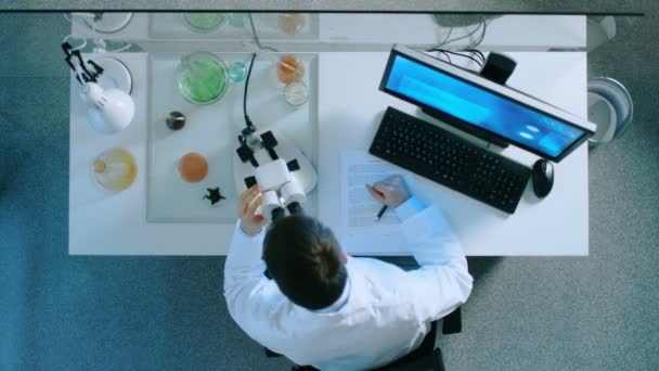 Вид зверху вченого шукає мікроскоп і аналізує інформацію з комп'ютером . — стокове відео