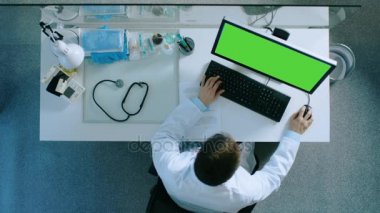 Top masasında oturan doktor görünümünü ve yeşil ekran ile bir bilgisayarda yazarak. Kağıt belge şarkı söylüyor.