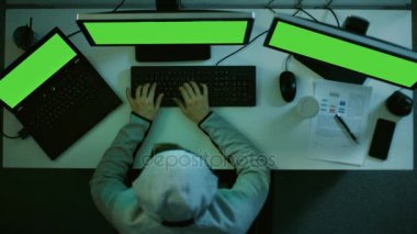 Üstten Görünüm uluslararası Datacenter kırma hacker. Onun iki monitörler ve dizüstü bilgisayar ile yeşil ekran vardır. Öz kötü amaçlı yazılım yapılmış kullanır.