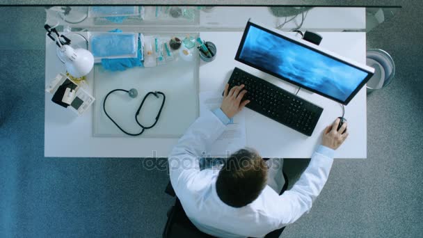 Top View of a Doctor Sitting at His Desk, Analysing Patient's X-Ray. He Writes Down Patient's Diagnosis Information on a Document. — Stock Video