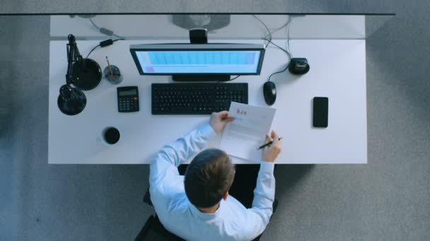Vue du dessus d'un employé de bureau assis à son bureau travaillant avec des feuilles de calcul sur son ordinateur personnel, signant des documents importants avec des graphiques et des graphiques. C'est tard le soir. . — Video