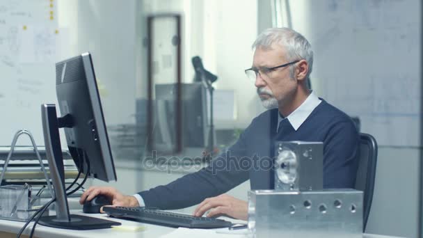 Ingenieurbüro. Chefingenieur an seinem Schreibtisch, einige technische Komponenten liegen auf seinem Schreibtisch. Sein Assistent arbeitet im Hintergrund am Schreibtisch. — Stockvideo