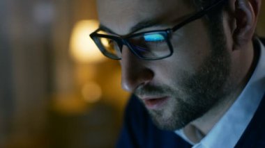 Bir adam evde close-up bir bilgisayarda çalışıyor. Ekran onlara yansıtır, gözlük takıyor.