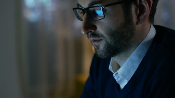 Närbild av en Man hemma arbetar på en dator. Han bär glasögon, skärmen reflekterar i dem. — Stockvideo