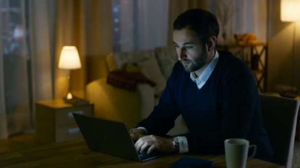 Респектабельно выглядящий мужчина средних лет работает над ноутбуком из своего дома. Его квартира имеет вид на большой город. Внутри тепло и уютно. . — стоковое видео