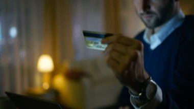 Yakın çekim bir adamın evde o tutar kredi kartı ve türlerini sayıya diz üstü. Internet üzerinde bir şey için ödeme. Rahat ve gökdelenler görünümü vardır onun evim.