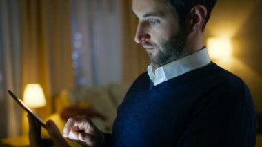 Saygın bir orta Close-Up Tablet bilgisayar kullanan adam yaşlı. Evde yalnızdır. Arka plan O'nun daire yapılır sarı renklerde şık görünüyor ve gökdelenler görünümü vardır.