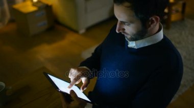 Saygıdeğer orta Tablet bilgisayar kullanarak masasında oturan adam yaşlı. Evde yalnızdır. Arka plan O'nun daire yapılır sarı renklerde şık görünüyor.