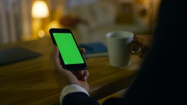 Eve bir adam üzerinde onun Resepsiyon ve kullanır Smartphone ile yeşil ekran oturur. Bir bardaktan içer. Onun daire sarı renklerde yapılır ve sıcak.