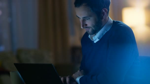 Middle Aged Man zit op zijn bureau werken op een Laptop. Op de achtergrond zijn appartement in gele tinten met een uitzicht op de wolkenkrabbers. — Stockvideo