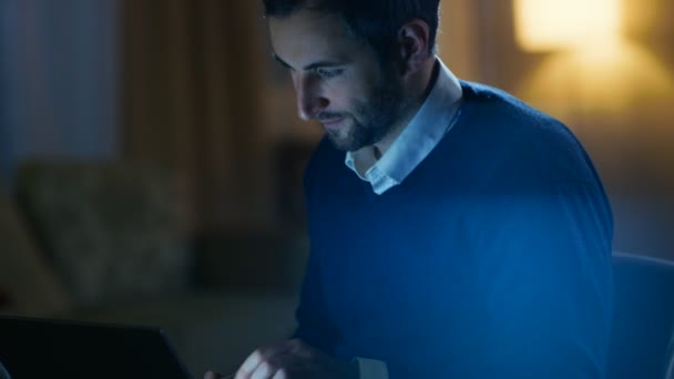 Hombre de mediana edad sentado en su escritorio trabajando en una computadora portátil. En el fondo su apartamento en tonos amarillos con una gran vista de la ciudad . — Vídeo de stock