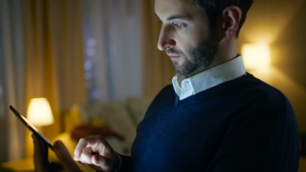 Close-up van een respectabele midden leeftijd Man met behulp van Tablet PC. Hij is thuis alleen. In de achtergrond zijn appartement gedaan in gele kleuren ziet er stijlvol en heeft wolkenkrabbers weergave. — Stockvideo