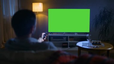 Büyük düz ekran Tv izlerken kanepede oturan adam arkadan görünüm bir orta yaşlı akşamları kanal uzaktan kumanda ile geçer. Akşam oldu.