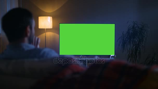 En la noche Vista trasera de un hombre de mediana edad sentado en un sofá viendo un televisor de pantalla plana grande . — Vídeo de stock
