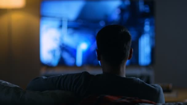 Back View of a Man Sitting on a Couch Watching Movie on His Big Flat Screen TV. — Stock Video