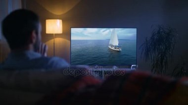 Bir adam oturan bir kanepe romantik film tarassut Yatçılık ve kamp ile tarih içinde O'nun büyük ekran televizyonda arkadan görünüşü. Akşam oldu. 