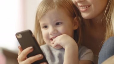 Güzel genç anne küçük kızıyla birlikte oturur ve ilginç bir şey Smartphone'da gösterir. 
