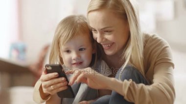 Güzel genç anne küçük kızıyla birlikte oturur ve ilginç bir şey Smartphone'da gösterir. Çocuk odası pembe ise tam Toys.
