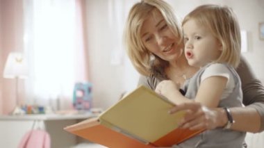 Sevimli küçük kız büyükannesinin kucağına oturur ve onlar çocuk kitabı okumak. Ağır çekim.