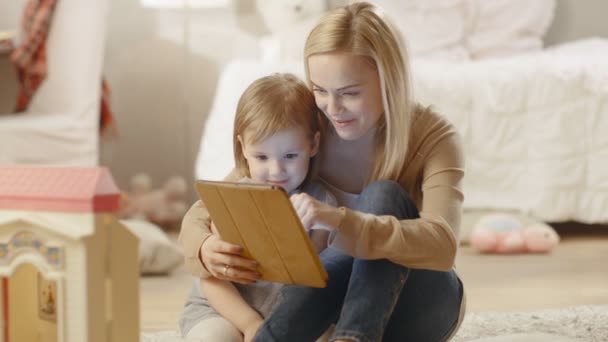 美丽的母亲和她的小女儿有一台平板电脑的好时间阅读儿童书。孩子们的房间充满了玩具. — 图库视频影像