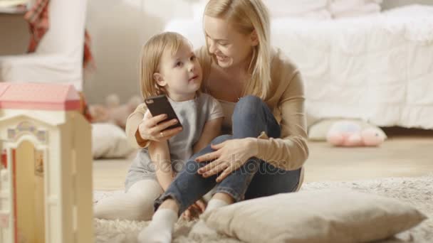 Прекрасна мати і її маленька донька добре розмовляють, мама тримає смартфон. Дитяча кімната повна іграшок . — стокове відео