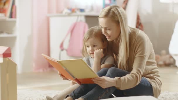 Die schöne junge Mutter liest ihrer süßen kleinen Tochter aus einem Kinderbuch vor. Kinderzimmer ist rosa und voller Spielzeug. — Stockvideo