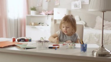 Onu tablo ve boya kalemi ile berabere, sevimli küçük kız oturuyor. Odası pembe, güzel çizimler duvarlarında birçok oyuncak etrafta asılı mı.