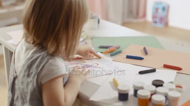 Sevimli küçük kız onu tablo ve berabere oturur. O sarı parmağıyla güneşi boya. Pembe ve rahat odası mı.