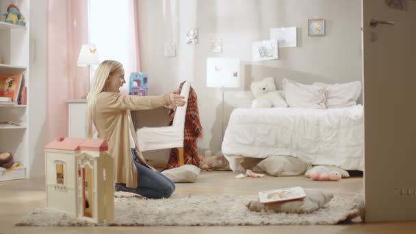 Jolie fille blonde court vers sa jeune mère et ils se câlinent. Chambre d'enfants est rose, a des dessins sur le mur et est plein de jouets. Mouvement lent . — Video