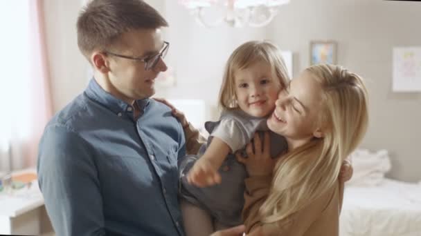 Jonge ouders houden dochter in hun armen en haar knuffel. Dochter golven naar de Camera. — Stockvideo